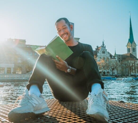 Man sitter i solen och läser en bok