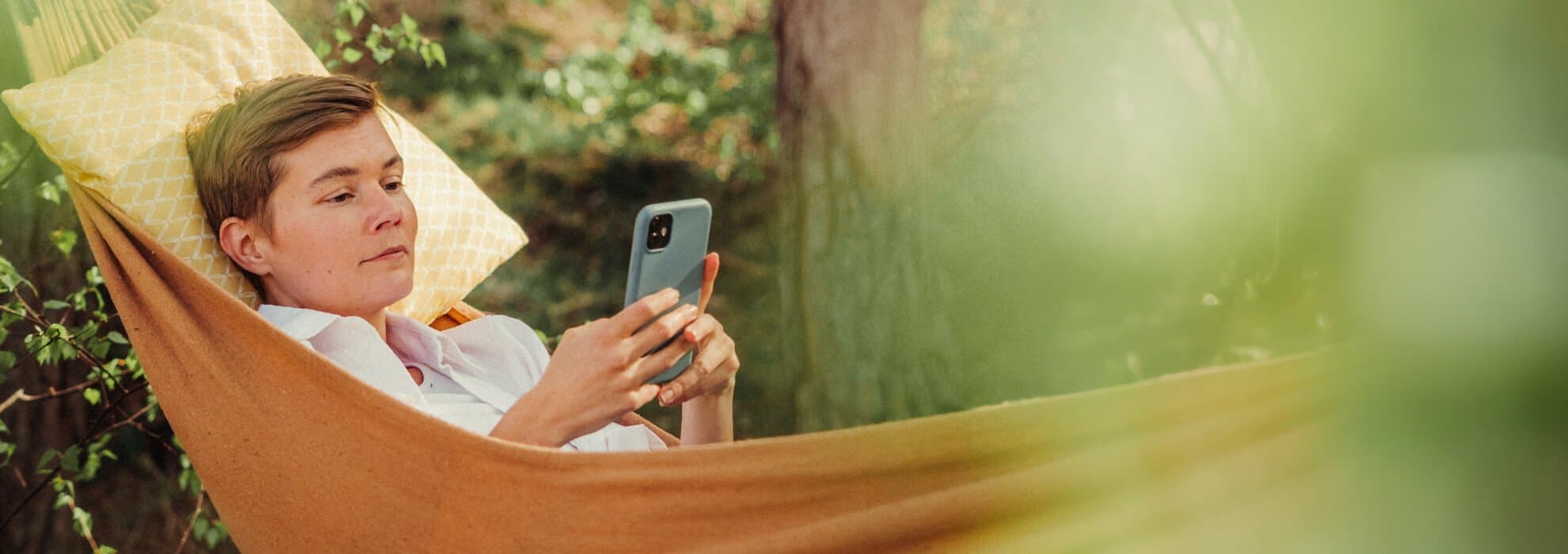 en kvinna som liggeri en hängmatta och scrollar med mobilen