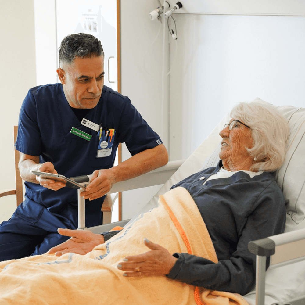 Kvinna ligger i säng och pratar med vårdpersonal